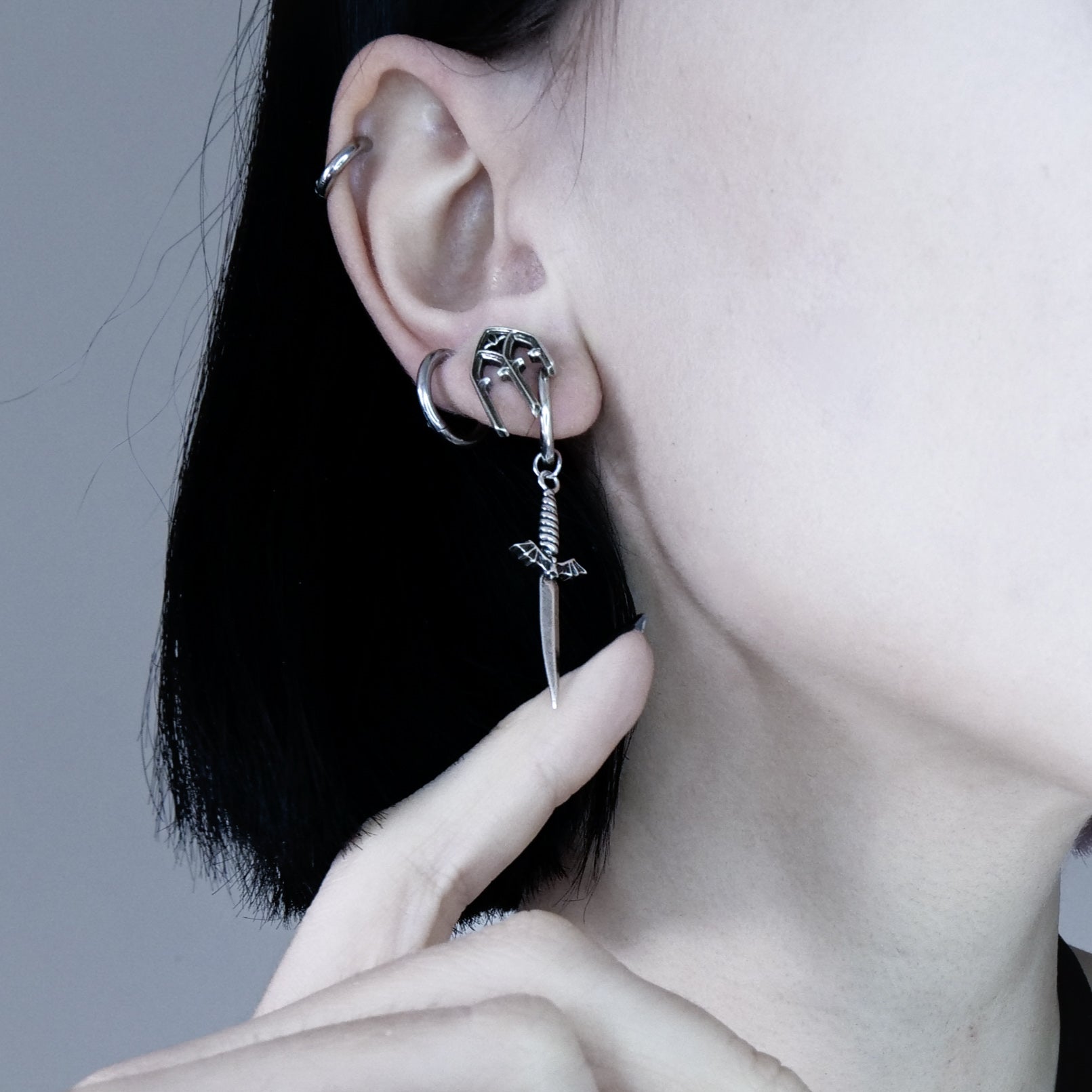 Side view of model wearing a silver-tone sword earring with winged top, styled with additional ear hoops