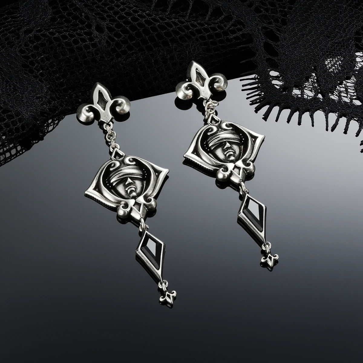 Antiqued silver-tone Blind Oracle Drop Earrings displayed from angled views against black lace on a reflective surface.