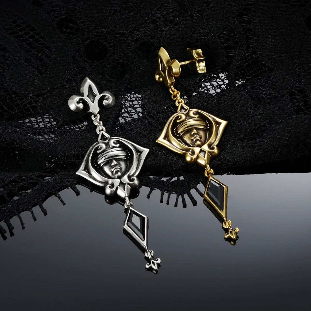 Antiqued silver- and gold-tone Blind Oracle Drop Earrings displayed together against black lace on a reflective surface.