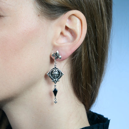 Close-up of an antiqued silver-tone Blind Oracle Drop Earring worn from the side, showing the blindfolded face and black zircon drop.