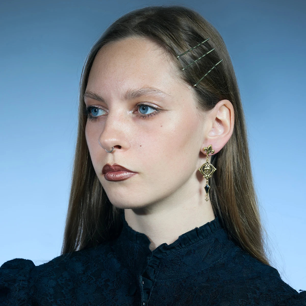 Three-quarter portrait showing a pair of antiqued silver-tone Blind Oracle Drop Earrings with black zircon drops.