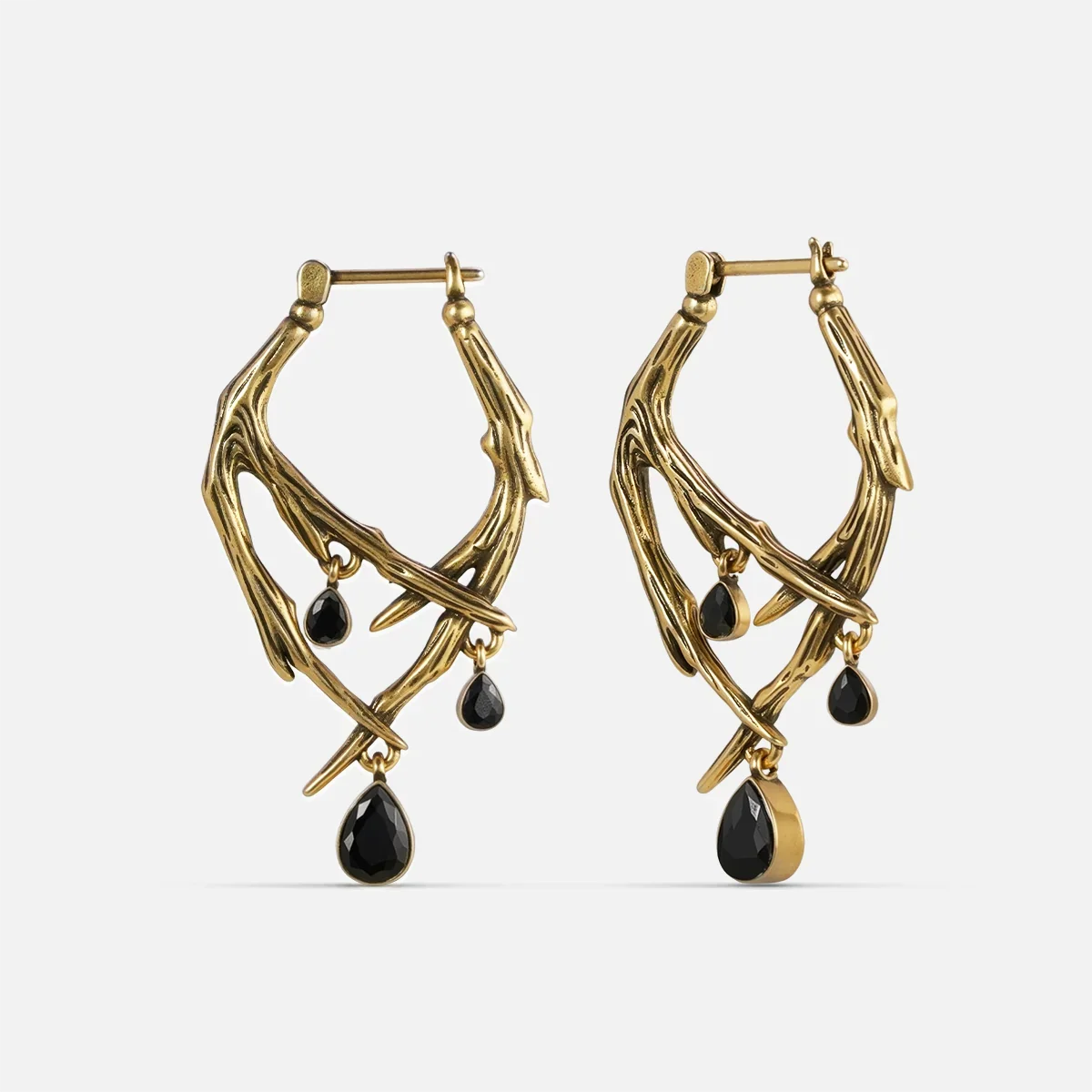 Gold-tone thorn-shaped hoop earrings pair with dangling black teardrop crystals, front view on white background