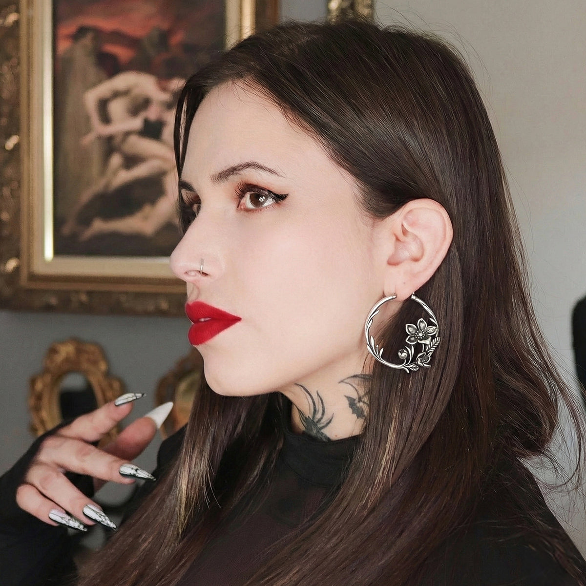 Model with dark hair wears a silver-tone hoop earring with a floral vine design, side profile view