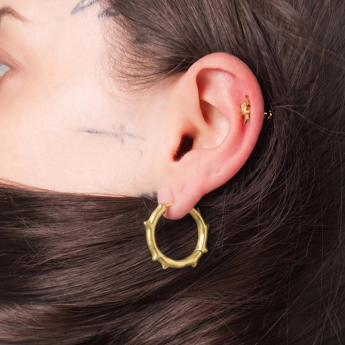 Model wearing gold Bramble Leaf Ear Studs with sharp leaf detail and titanium finish