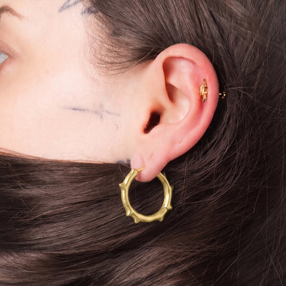 Model wearing gold Bramble Leaf Ear Studs with sharp leaf detail and titanium finish