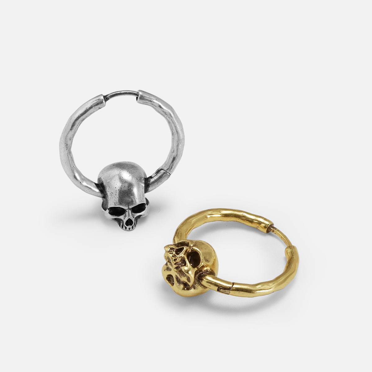 Brave skull earrings shown in gold and silver from a side angle, highlighting the skull detail and hoop shape