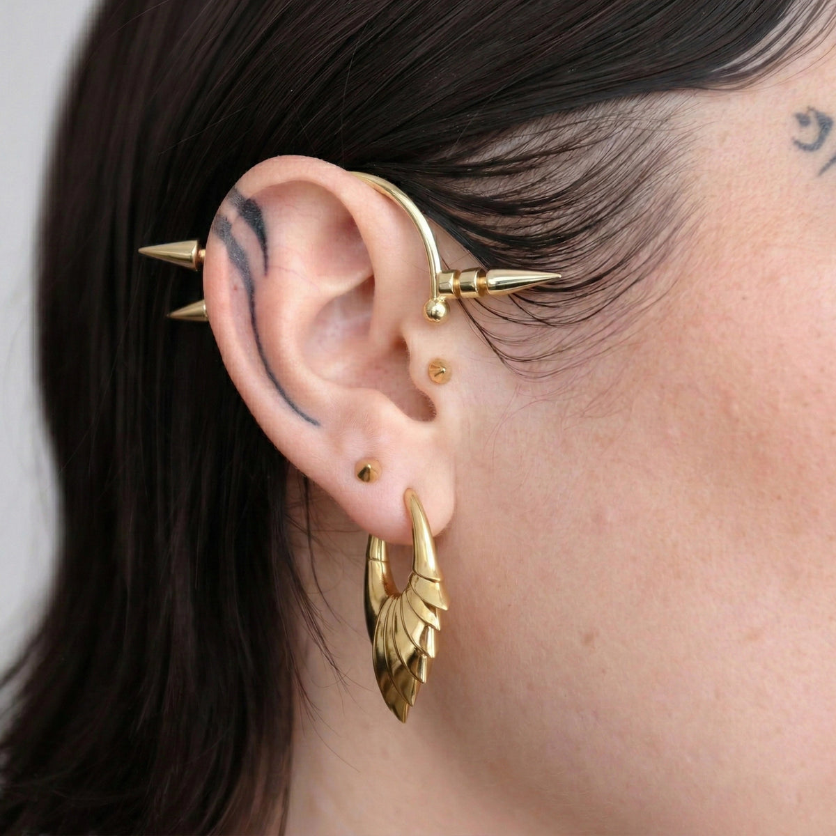 Model wearing a gold-tone wing hoop earring with a spiked ear cuff and studs