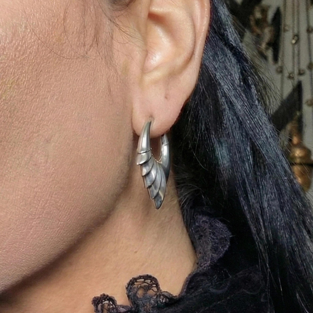 Close-up of a model wearing a silver-tone wing hoop earring on the ear