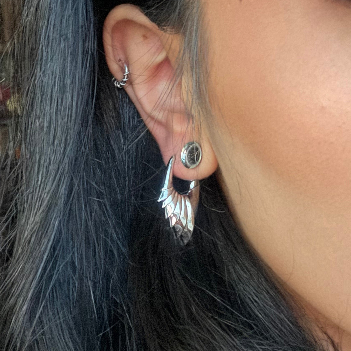 Model wearing a silver-tone wing hoop earring alongside a stud and cartilage hoop