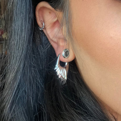 Model wearing a silver-tone wing hoop earring alongside a stud and cartilage hoop