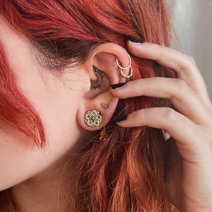 Close-up of a model wearing a gold-tone rose window ear plug alongside hoops and stud earrings