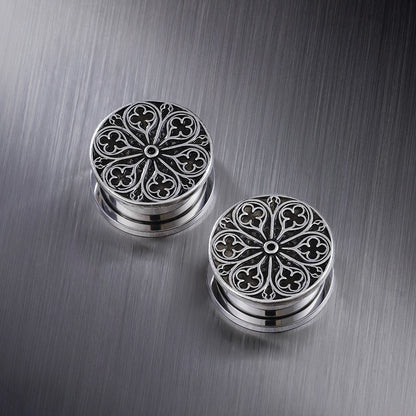 Pair of silver-tone ear plugs with a detailed cathedral rose window pattern on a metal surface