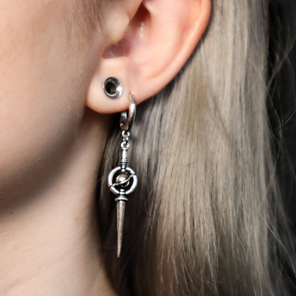 Silver-tone hoop earring with spike and orbit ring pendant worn on a model with light blonde hair