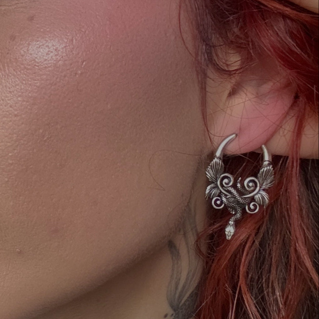Close-up of a model wearing a silver-tone serpent hoop earring with wing details, hair falling over the ear