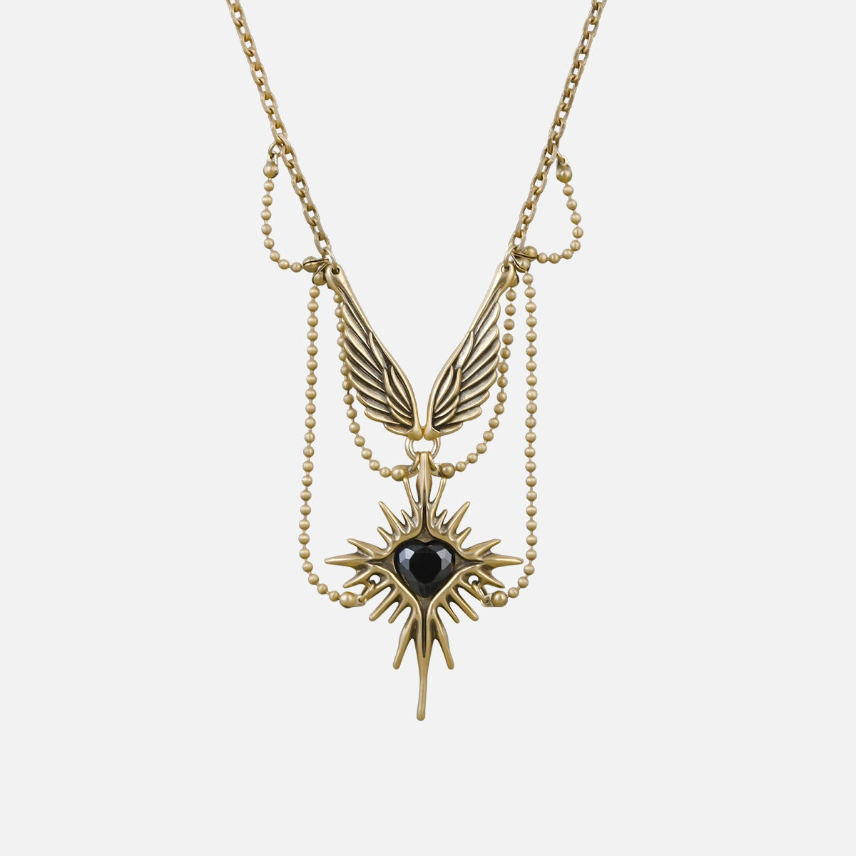 Gold-tone necklace featuring layered chains, wings and a starburst pendant with black stone, laid flat on white background
