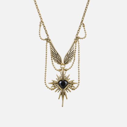 Gold-tone necklace featuring layered chains, wings and a starburst pendant with black stone, laid flat on white background