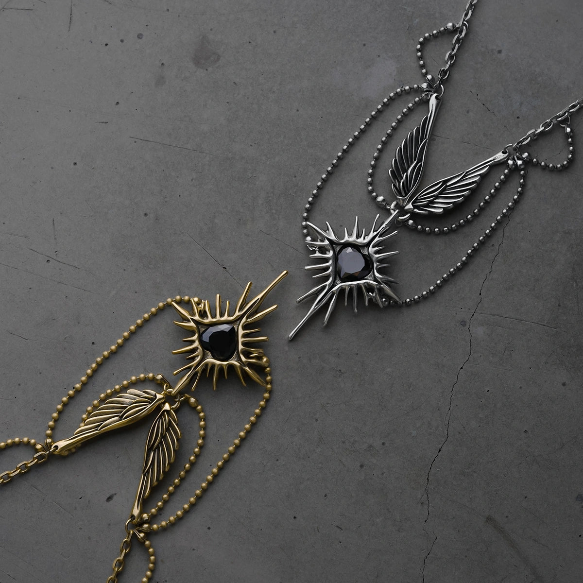 Gold and silver-tone Celestial Starburst Wings necklaces arranged on a dark textured surface