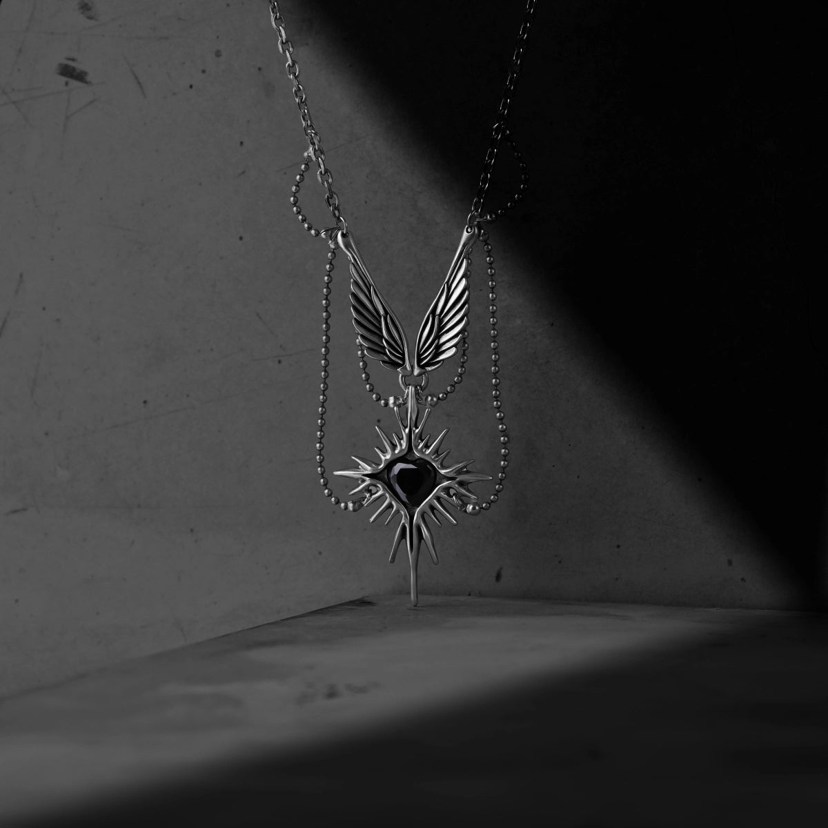 Silver-tone Celestial Starburst Wings necklace hanging against a shadowed gray backdrop