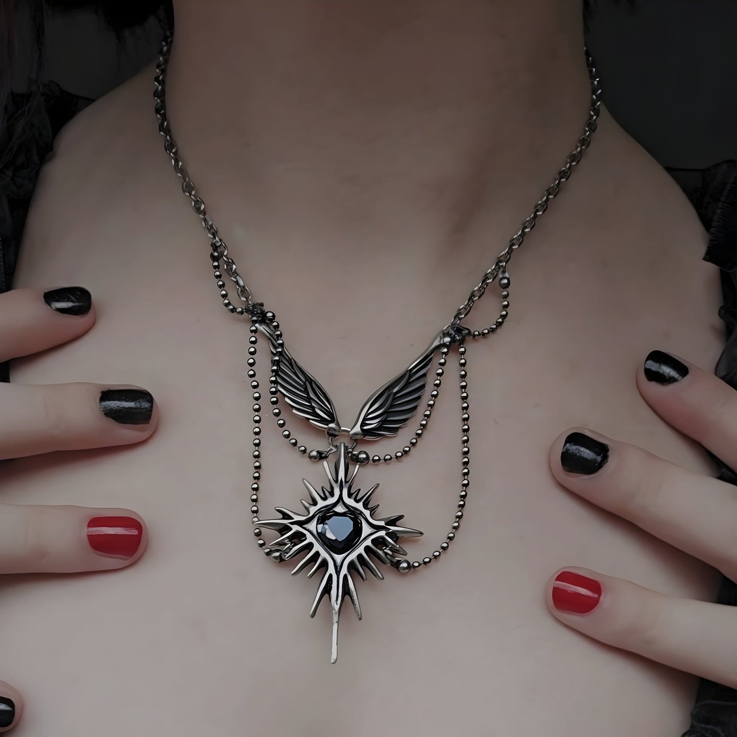 Silver-tone wings and starburst pendant necklace with black stone worn close to chest, hands with painted nails nearby
