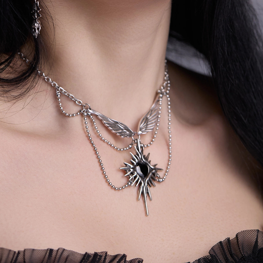 Silver-tone starburst wings necklace with black stone pendant worn on model's neck, close view