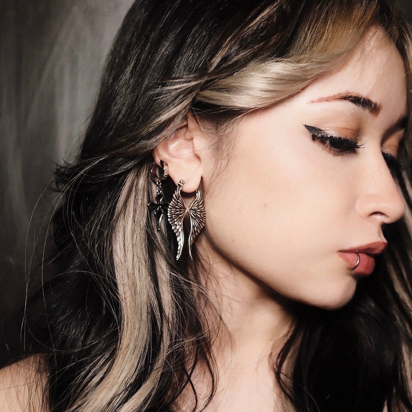 Model with dark hair wearing a small hoop paired with a dangling wing earring