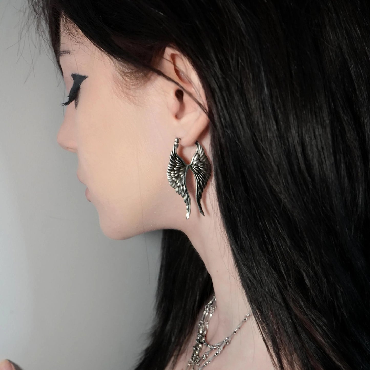 Model wearing silver Celestial Wing Earrings with layered feather wing design and elongated silhouette