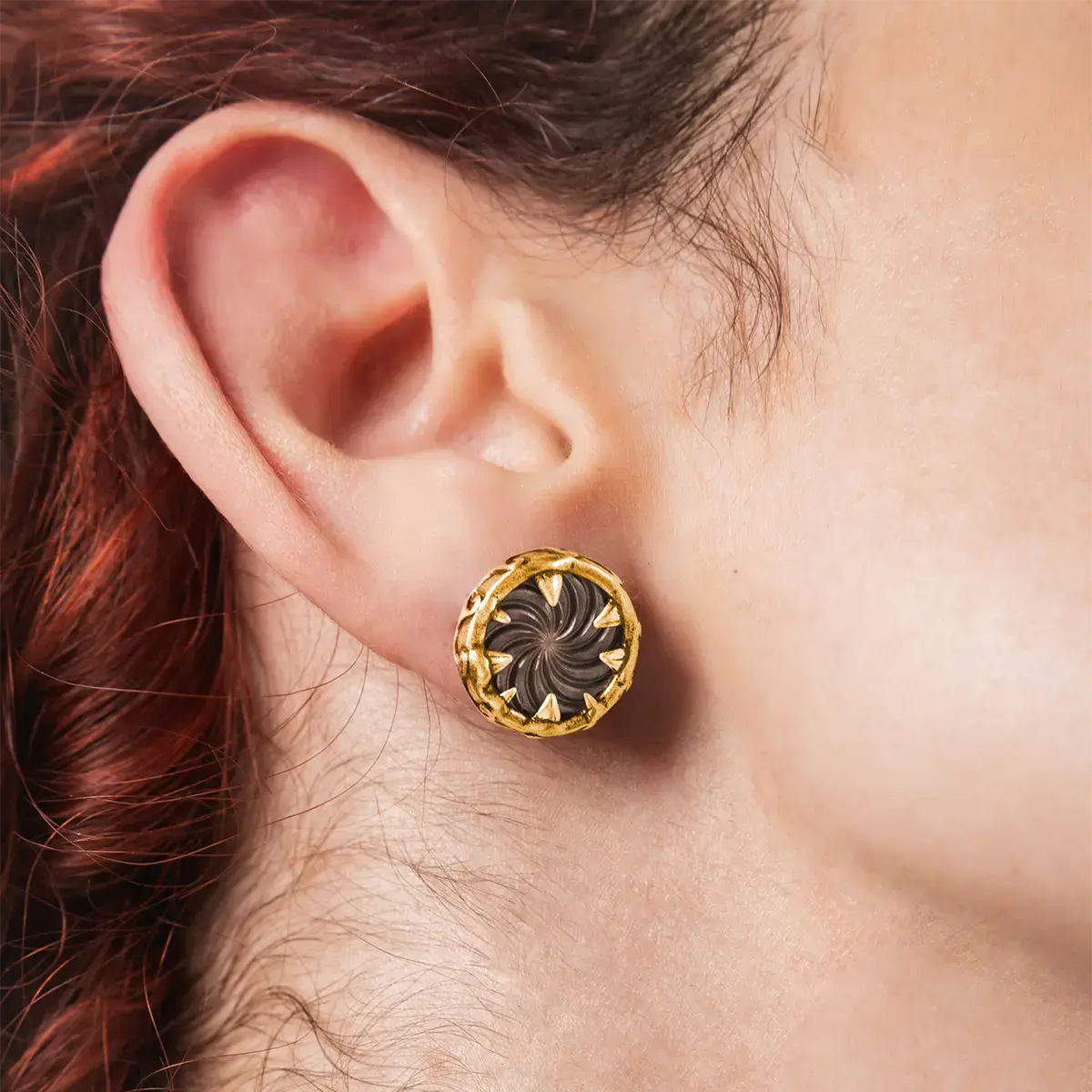 Woman wearing antique brass Charybdis Maw stud earrings featuring an abalone shell spiral center
