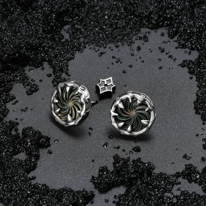 Silver Charybdis Maw Ear Studs displayed on black sand, highlighting the abalone shell spiral center and carved gothic rim details.