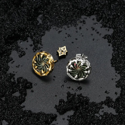 Silver and gold Charybdis Maw Ear Studs displayed on black sand, showing the swirling abalone shell centers and dark ocean-inspired styling.