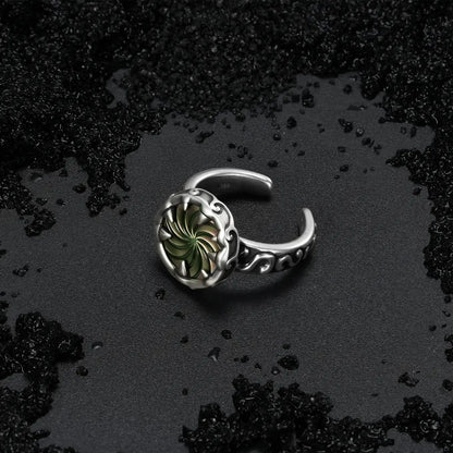 Charybdis Maw Ring placed on a dark wet surface, highlighting the abalone shell center and silver wave-like ring setting.