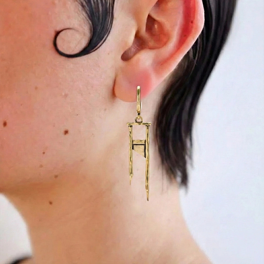 Model wearing a gold Chic Guillotine hoop earring with long geometric drop