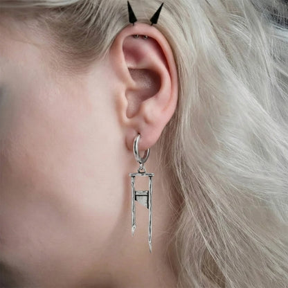 Silver-tone hoop earring with a guillotine-shaped dangling charm, worn on model's ear, close-up side view
