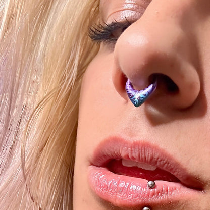 Close-up of a septum clicker with a purple and blue swirl finish worn in the nose, styled with a labret piercing