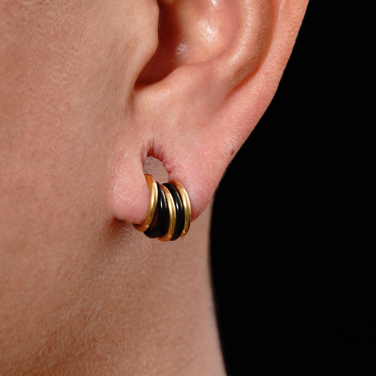 Close-up of stacked hoop earrings in black and gold-tone finishes worn in an ear