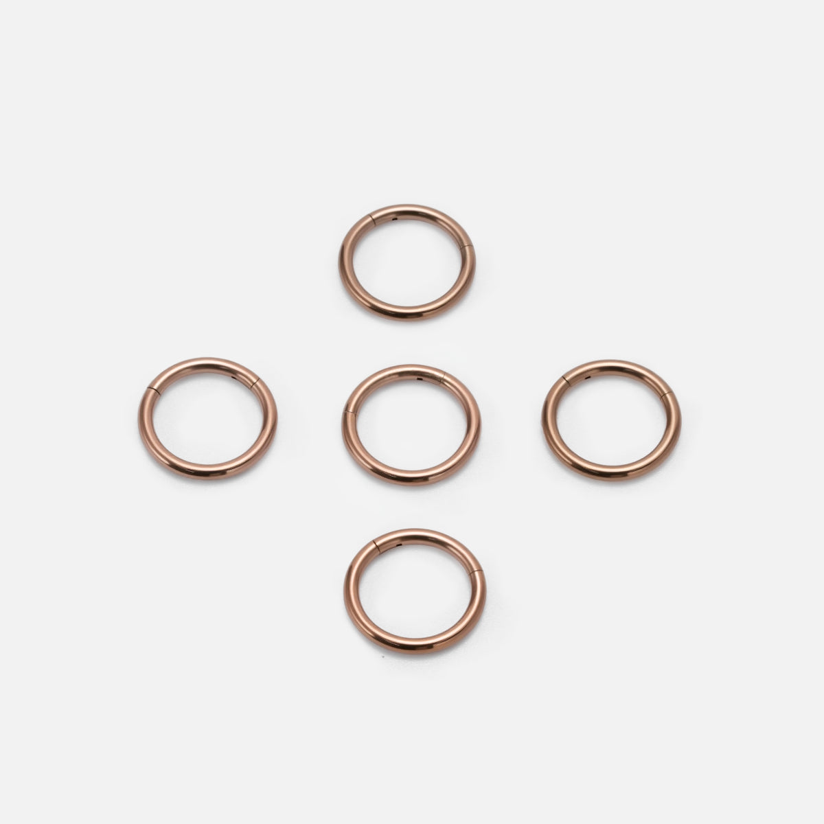 Five rose gold Chromatic Loop rings arranged on a white background