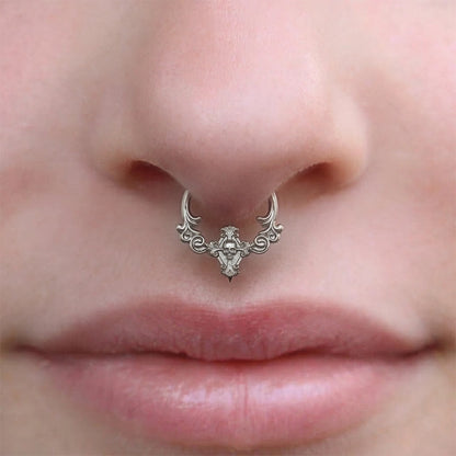 Silver-tone septum clicker with scrollwork and skull detail worn on a model's nose, close-up front view