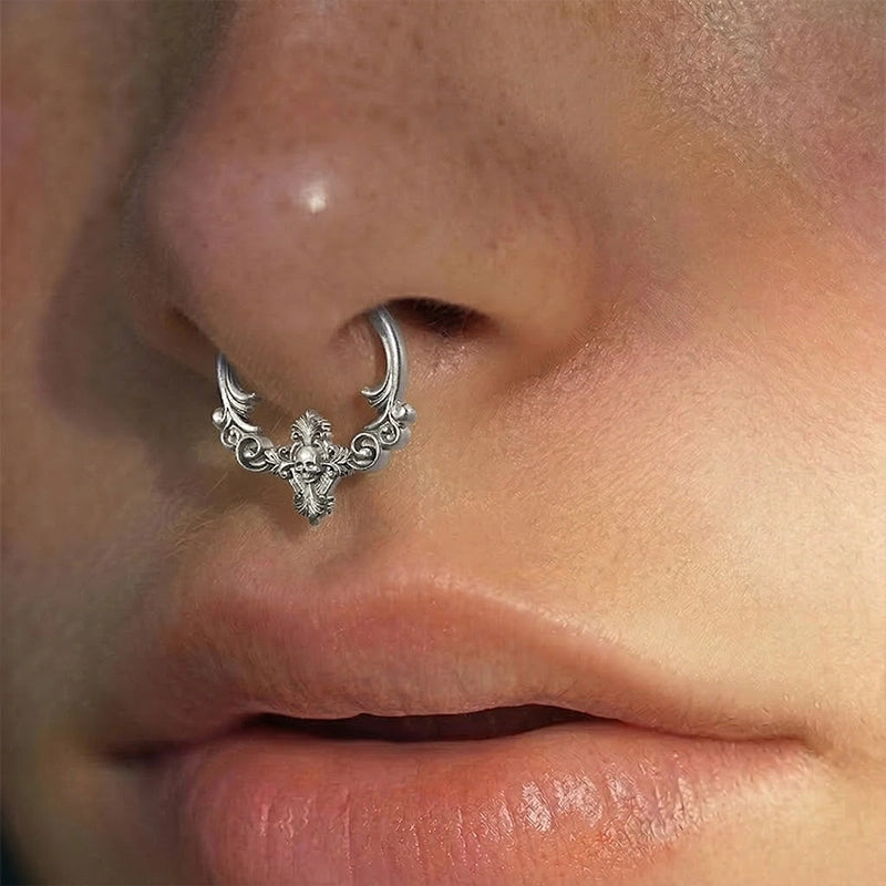 Silver-tone septum ring with filigree scrolls and skull design worn on a model's nose, close-up side angle