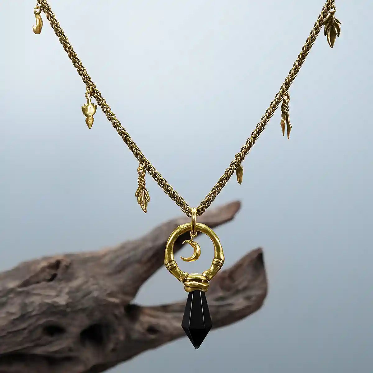 Gold Crescent Ward Necklace with black obsidian pendant photographed on driftwood