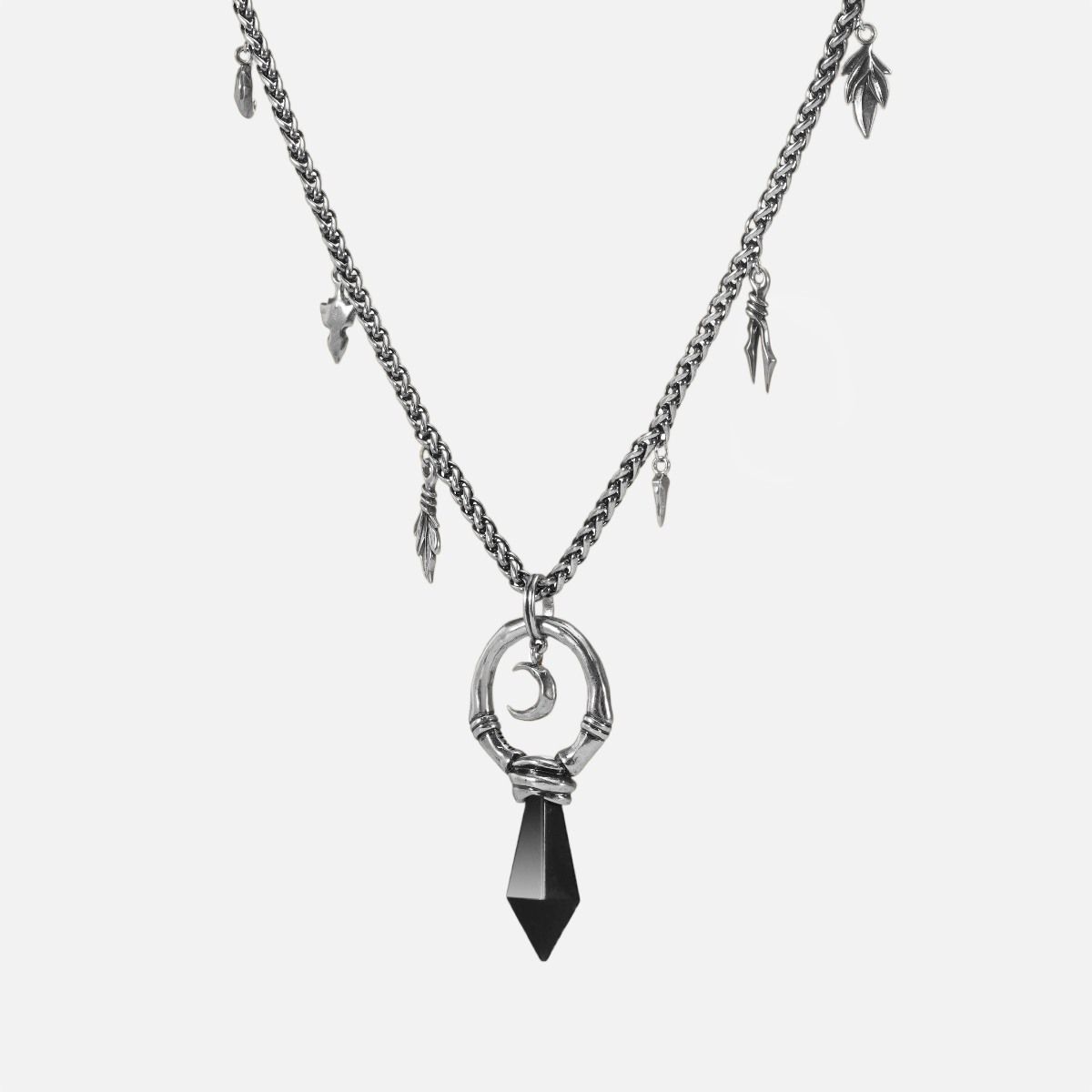 Close-up product view of the silver Crescent Ward Necklace, featuring a black obsidian spike, crescent moon charm, bone ring centerpiece, and relic-like chain accents.