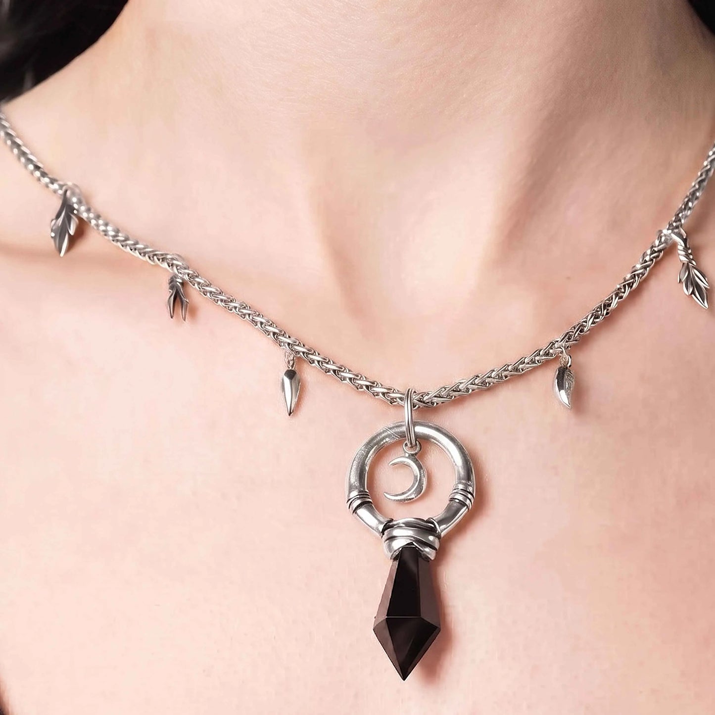 Model wearing the silver Crescent Ward Necklace with black obsidian spike pendant, crescent moon charm, and gothic forest-inspired chain details.