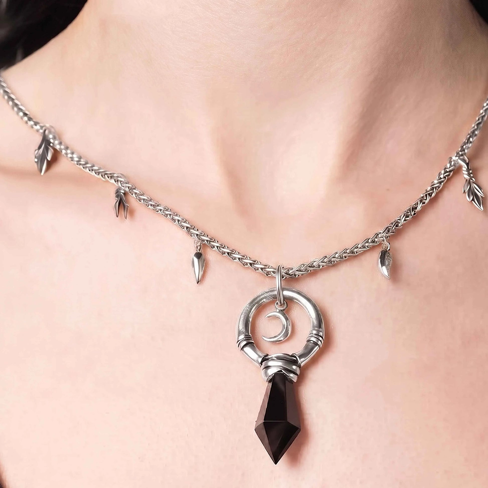 Model wearing the silver Crescent Ward Necklace with black obsidian spike pendant, crescent moon charm, and gothic forest-inspired chain details.