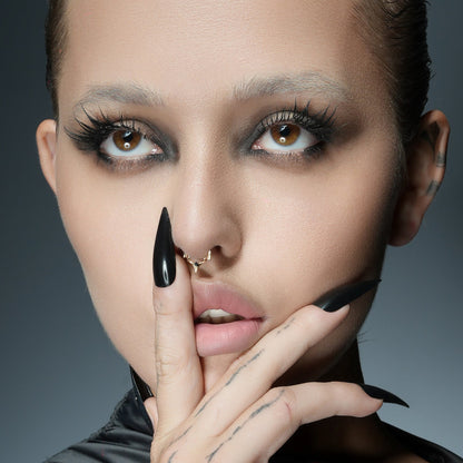 Model with dark makeup wearing a gold-tone spiked septum ring, hand with black nails near face