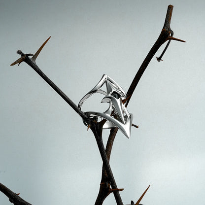 Silver-tone Crest Shield ring balanced on a thorn branch, showing its open pointed geometric face
