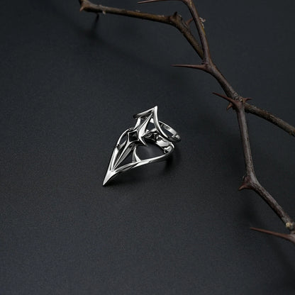 Silver-tone Crest Shield ring resting beside a thorn branch on a matte black surface