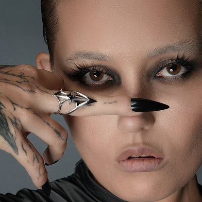 Close-up of model's face with a silver-tone crest shield ring worn on a finger held near one eye