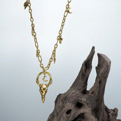 Gold Crow Ward Necklace photographed on driftwood with bird skull pendant and crescent moon charm