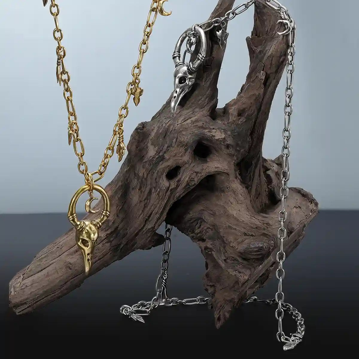 Crow Ward Necklace in gold and silver displayed on driftwood with gothic forest inspired styling