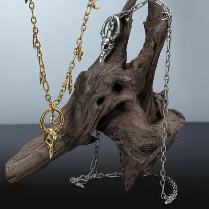 Crow Ward Necklace in gold and silver displayed on driftwood with gothic forest inspired styling