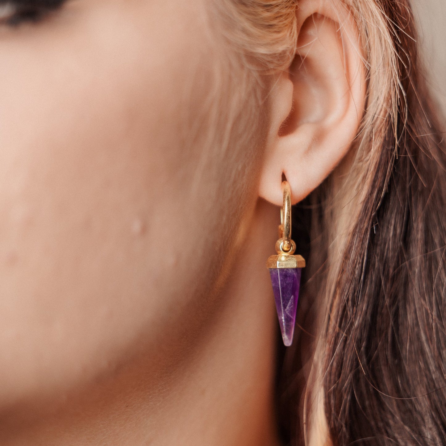 Gold-tone Crystal Prismatic hoop earring with a purple faceted point worn in side profile