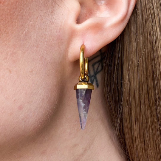Close-up of a gold-tone Crystal Prismatic hoop earring with a tapered purple crystal pendant